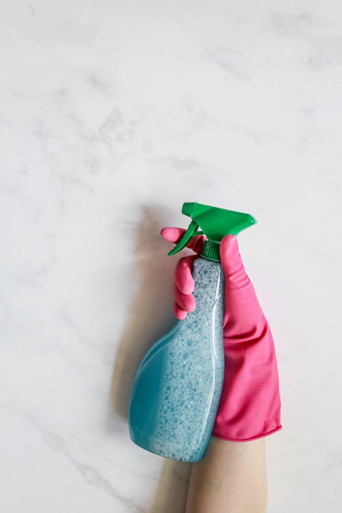 services-02 Close-up image of a hand in a pink glove holding a spray bottle against a white background.